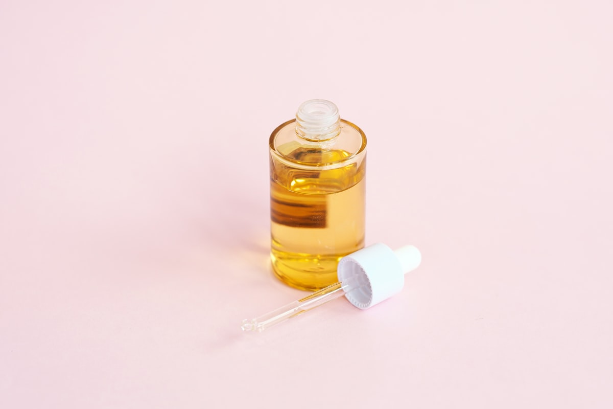 A label-free amber glass serum bottle beside an open white dropper on a soft pink surface, no identifiable person and no readable brand or logo, a clean minimalist skincare still life for the piece on record Korean cosmetics exports and the first US-listed K-beauty ETF