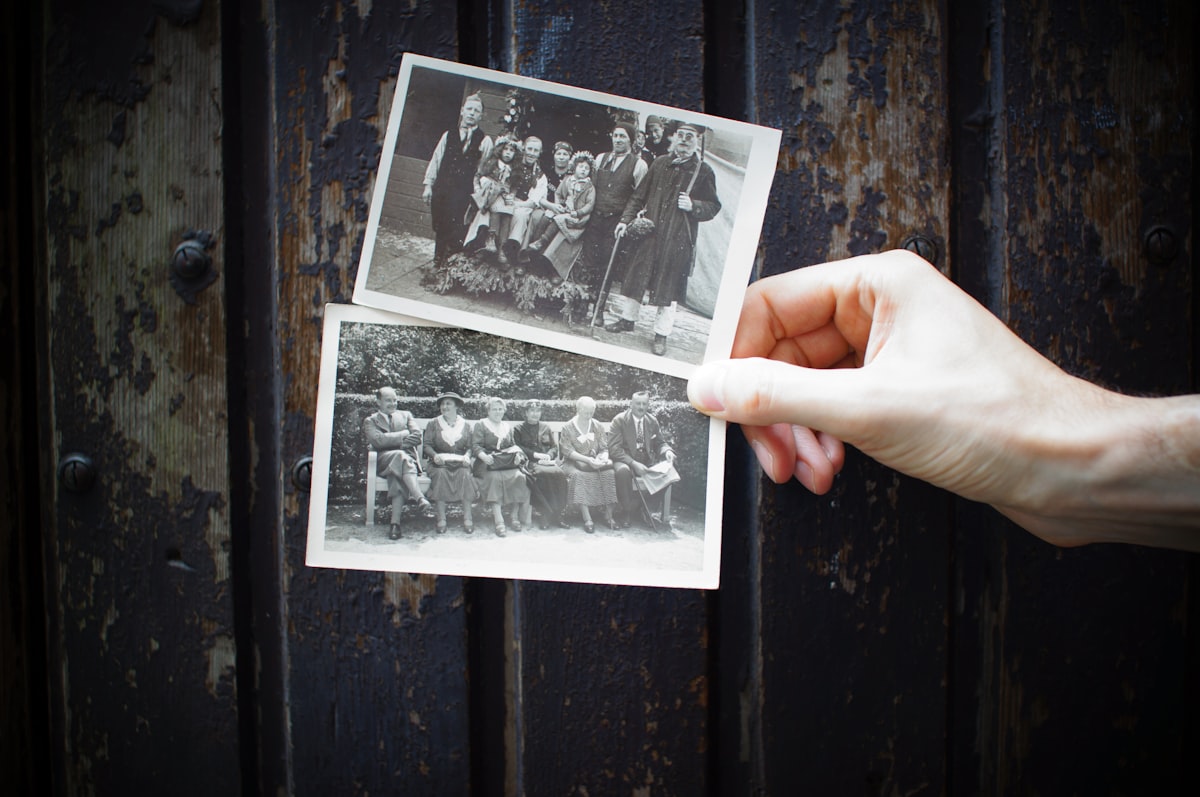 An unidentified hand holding two old black-and-white family photographs of unnamed, unidentifiable people, no living person's face and no brand, for the piece on chatbots trained on a dead person's messages, voice, and photos without their consent