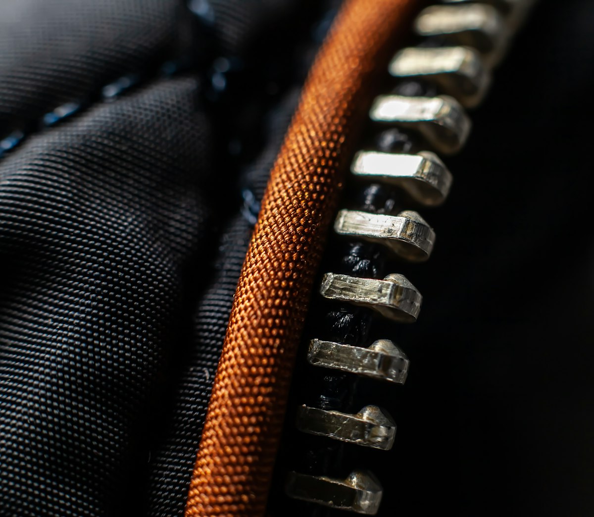 A macro close-up of a black and orange jacket zipper, no identifiable person and no readable brand name or logo, echoing the piece's lede about turning a fleece inside out to check whether the zip was recycled, for the story on the ASA banning fashion ads over unqualified recycled claims