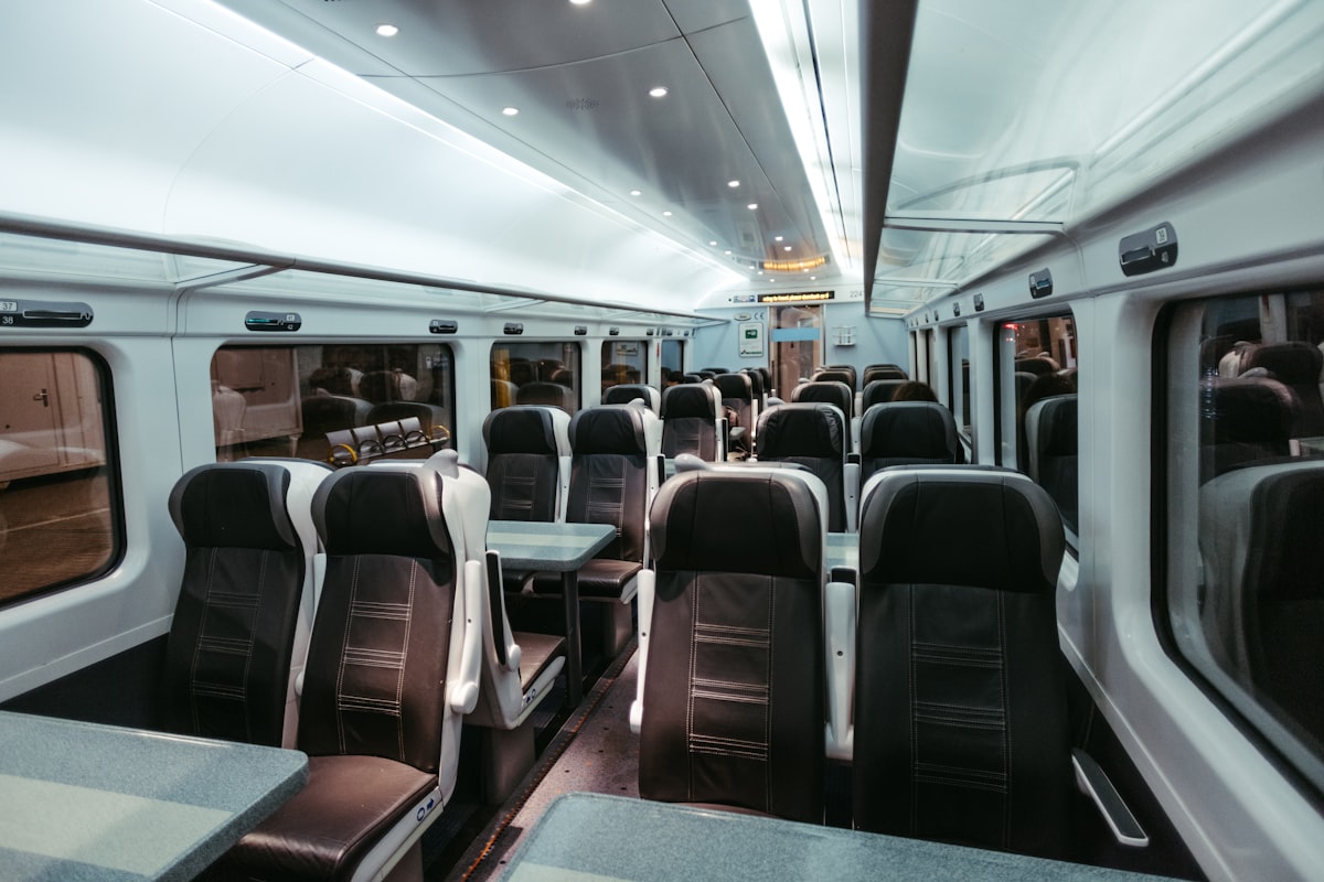An empty train carriage seen down the aisle, rows of seats and tables with no passengers in frame, no identifiable person and no operator livery, logo or readable branding, for the piece on rules against playing phone audio aloud that were already on the books