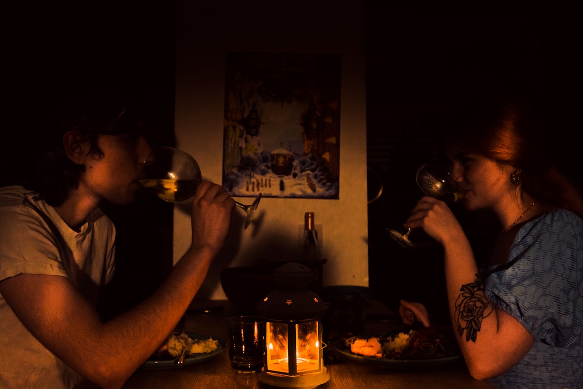 A man and a woman sitting across a small table with glasses of wine, no bill in frame and no clearly identifiable faces, for the piece on who pays on a date and the inviter-pays rule