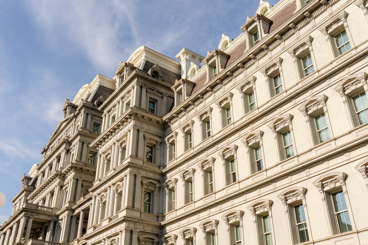 A grand ornate Second Empire stone building facade with mansard roofs and rows of pedimented windows rising against a blue sky, no identifiable person and no readable brand or logo, its architecture legible as a monumental old palace rather than a modern hotel room, for the piece on heritage landmarks being turned into hotels