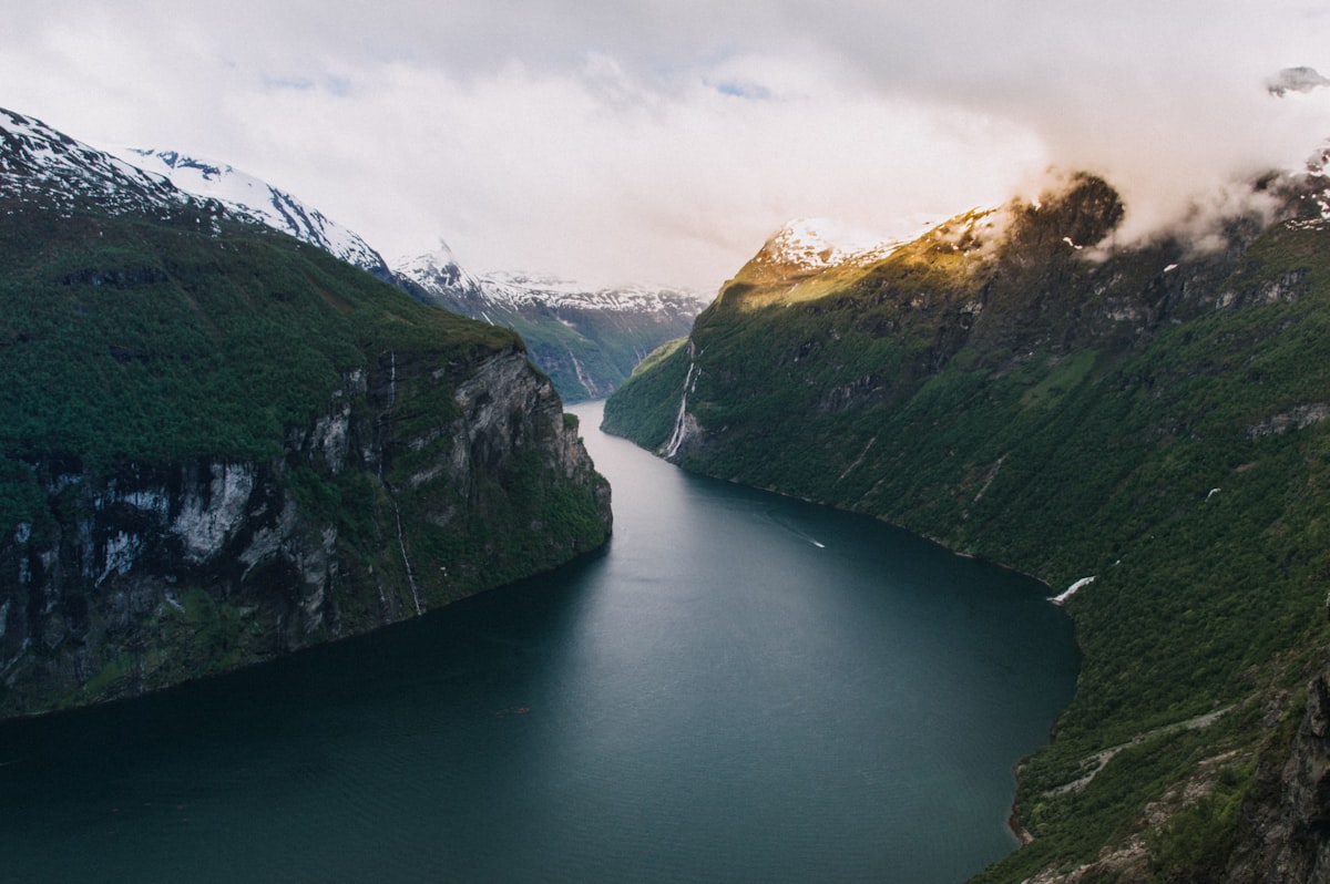 A Norwegian fjord between steep mountains under open summer light, no identifiable people, for the piece on booking Norway for July and Santorini for October
