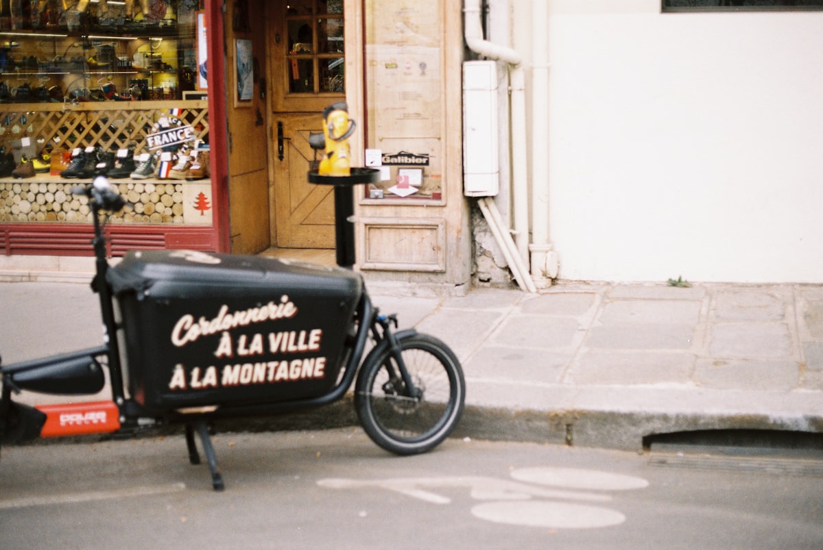 A black box cargo bike parked on a city street outside a shop, no identifiable people and no prominently featured bike brand, for the piece on e-bikes and cargo bikes substituting for car trips
