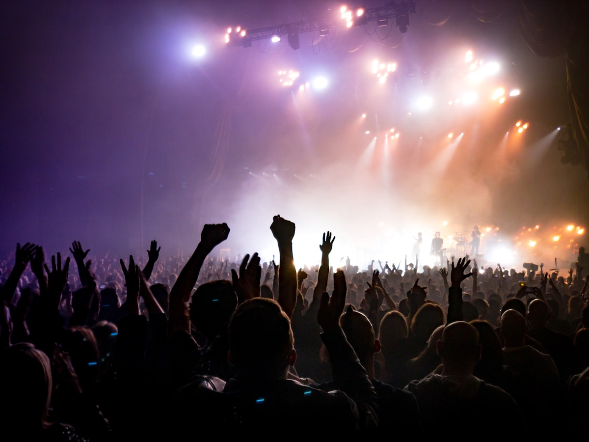 A concert crowd silhouetted before a brightly lit stage, no identifiable individuals and no readable brand, for the piece on the K-shaped live-music market