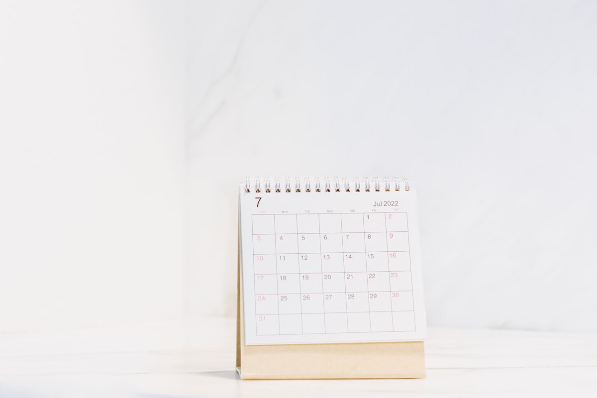 A minimal spiral-bound desk calendar showing a month on a white marble surface with generous empty space, no identifiable people and no readable brand names or logos, for the piece on the four-day week and the price of the fifth day