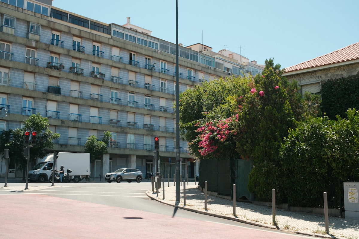 A mid-century residential apartment block with tiled facade and balconies on an ordinary street in Benfica, Lisbon, with parked vehicles and flowering shrubs, no identifiable person as the subject and no readable brand or logo in frame, for the piece pricing ten remote-work bases for 2026